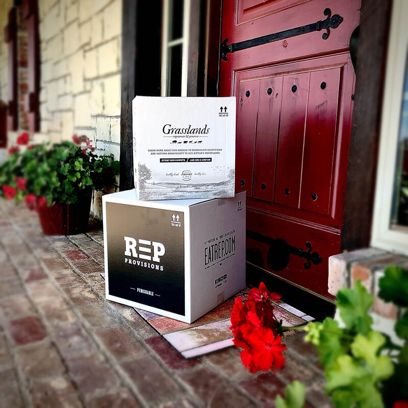 A REP Provisions box delivered to a brick porch beside a red front door and potted flowers