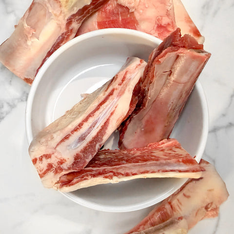 Raw grass-fed beef rib bones for dogs in and around a white bowl on marble