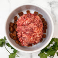 Raw grass-fed ground beef for dogs served over dog food in a white bowl