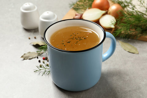 Mug of golden bone broth with onions, herbs and spices